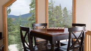 A dining area with a wooden table and chairs, large windows offering a view of a forest and mountains. - Wrap-Deck Hot Tub w/ Mt. Sherman Views - Fire Pit, Wildlife (Fairplay)