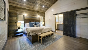 Quarto com teto de madeira, cama com cabeceira, um banco e um tapete.