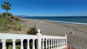 Une plage bordée d’une clôture blanche, avec des palmiers et une vue dégagée sur l’océan.