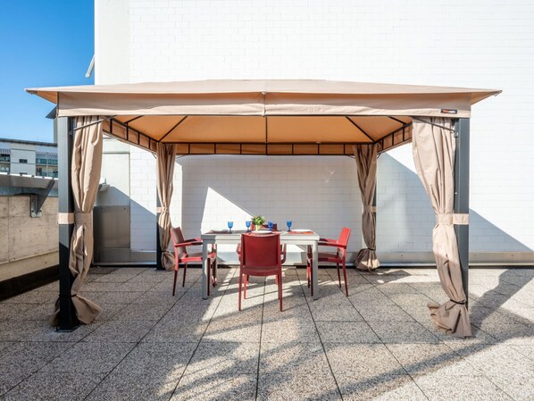 Relax in a shaded patio area with a table and four chairs, surrounded by a canopy and a small potted plant.