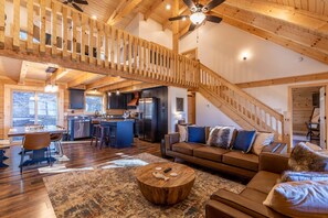 A spacious living area with a wooden staircase, a kitchen, and a dining area.