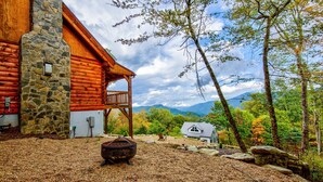 A log cabin with a stone chimney, a wooden deck, and a view of a mountain range. - Ursa Minor - Long Range Views, hot tub, Peloton, more at Beautiful 3bd/2ba home on Sugar (Banner Elk)