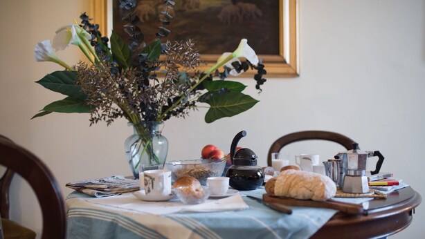 A dining table with a vase of flowers, a teapot, a croissant, and a bowl of fruit. - Beautiful apartment for 4 people with WIFI, TV and panoramic view (Florence)