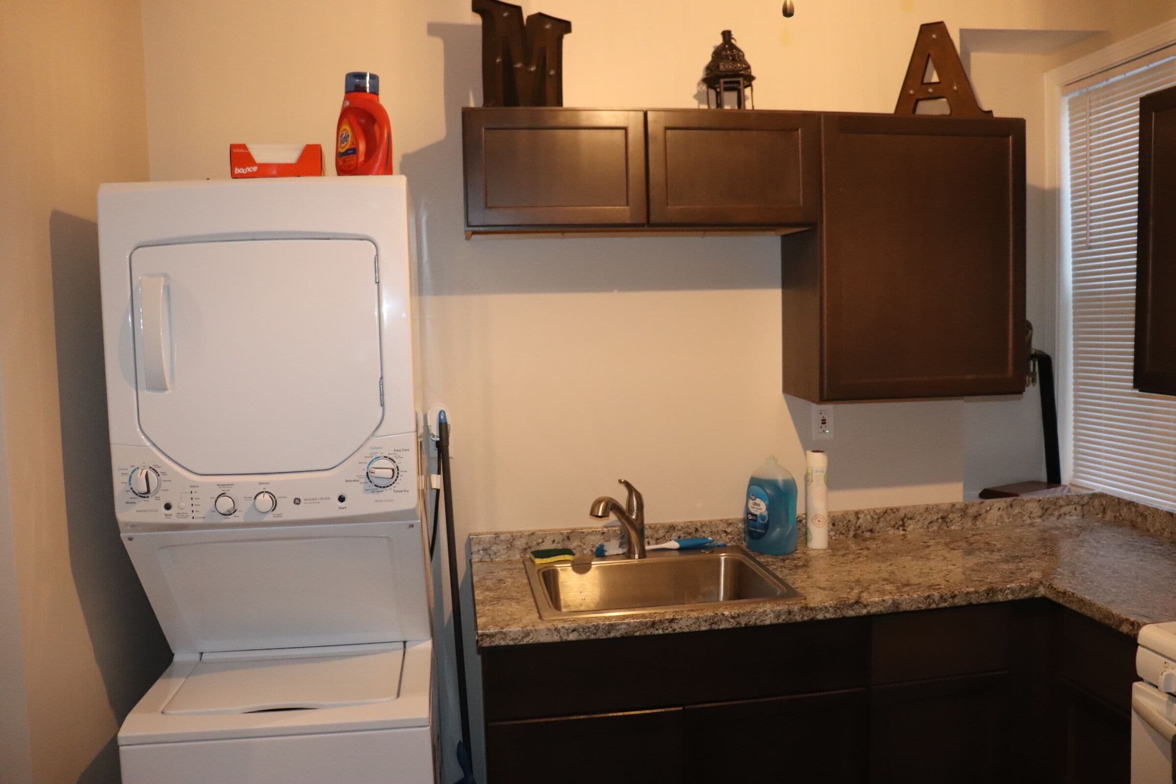 A compact kitchen with a built-in washer and dryer, a granite countertop, and dark wooden cabinets.
