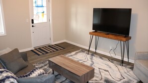 A living room with a sofa, a coffee table, a TV on a wooden stand, and a patterned rug.