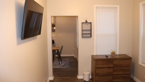 A hallway with a wooden dresser, a framed picture, and a door with blinds.