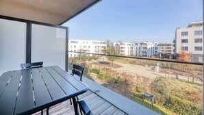 A balcony with a table and chairs, overlooking a residential area with modern buildings and a clear sky.
