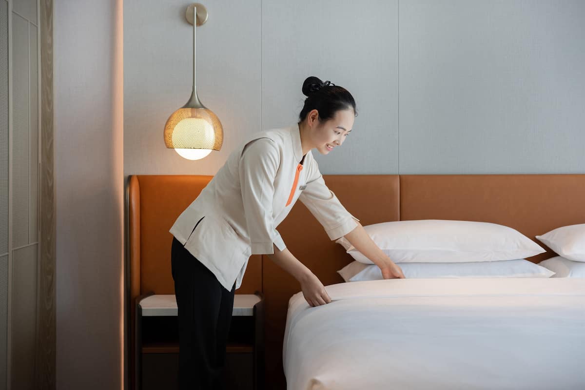 A hotel room with a neatly made bed, a bedside table, and a hanging light fixture.