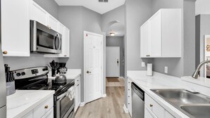 A modern kitchen with white cabinetry, a stainless steel sink, and a microwave. - Ultimate 3 Bedroom Condo on Windsor Palms Resort, Orlando Condo 6143 (Orlando)