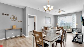 A dining area with a wooden table, chairs, and a chandelier. There is a ceiling fan and a window with curtains. - Ultimate 3 Bedroom Condo on Windsor Palms Resort, Orlando Condo 6143 (Orlando)