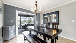 A dining room with a dark wooden table, chairs, and a chandelier. There is a bench in front of the table and a cabinet to the left. - Luxury Contemporary Style House on Charlotte Harbor Area, Charlotte County House 5819 (Charlotte County)