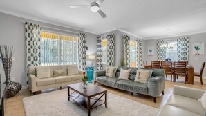 A spacious living room with a beige sofa, a grey sofa, a wooden coffee table, and a dining area with a wooden table and chairs.