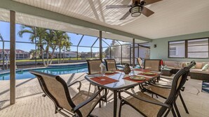 Un espace extérieur abrité, aménagé pour les repas, avec vue sur la piscine, comprenant une table avec des chaises et un ventilateur de plafond.