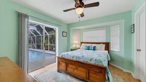 A bedroom with a bed, a ceiling fan, a window with blinds, and a sliding glass door leading to a pool area. - Perfect 3 Bedroom House on Charlotte Harbor Area, Charlotte County House 5827 (Charlotte County)