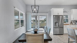 Una cocina moderna con refrigerador de acero inoxidable, armarios blancos y un comedor con mesa y sillas de madera.