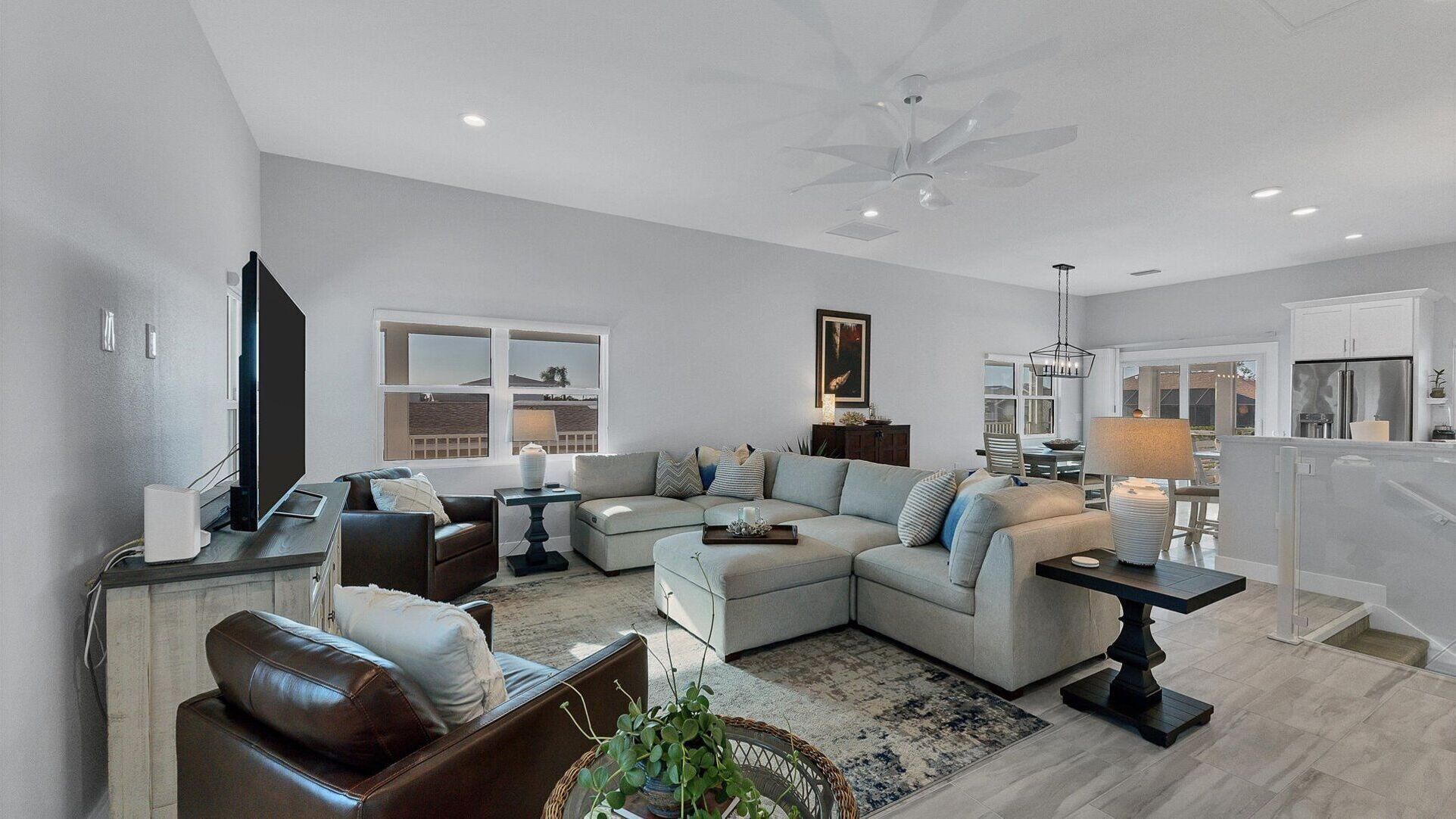 A modern living room with a sectional sofa, a flat-screen TV, and a dining area with a chandelier.