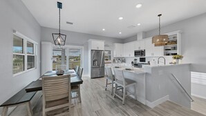 Cocina moderna con armarios blancos, una isla central, electrodomésticos de acero inoxidable y una zona de comedor con vistas.