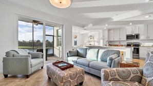 Amplia sala de estar con un gran ventanal corredero que da a un balcón, una cocina moderna con armarios blancos y un comedor con candelabro.