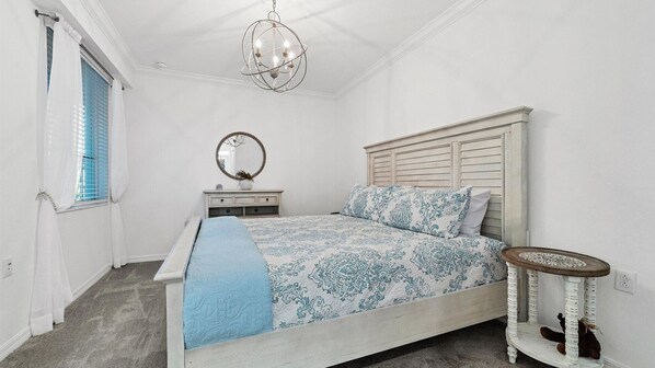 Un dormitorio con cama, cómoda, espejo, una mesa redonda y una lámpara colgante.