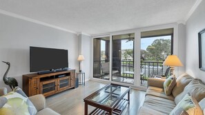 Relax in this stylish living room with a flat-screen TV, comfortable sofa, and sliding glass doors leading to a balcony with a water view.