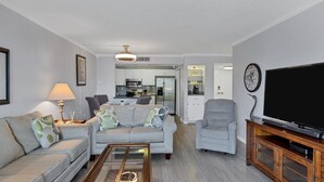A living room with a sofa, armchair, and coffee table. There is a television on a wooden stand and a kitchen in the background. - Ultimate 2 Bedroom Condo on Charlotte Harbor Area, Charlotte County Condo 5840 (Charlotte County)