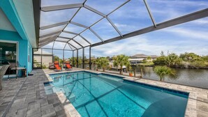 A swimming pool with a covered patio area, red lounge chairs, and a view of a body of water and surrounding landscape.