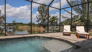 Zona de piscina con cerramiento de vidrio, dos sillones blancos y vistas a un lago y árboles.