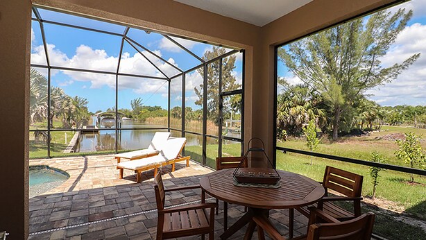 Un patio techado con mesa y sillas, con vistas a una piscina y abundante follaje.