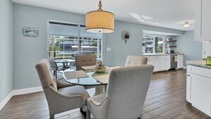 Una cocina moderna con armarios blancos, un comedor con mesa y sillas de vidrio, y un ventanal con vistas al exterior.