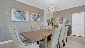 Ein Esszimmer mit einem Holztisch, sechs gepolsterten Stühlen, zwei abstrakten Gemälden, einer modernen Chandel und einer weißen Tür.