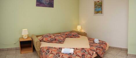 A room with a bed, two bedside tables with lamps, a wall-mounted air conditioner, and two framed pictures.