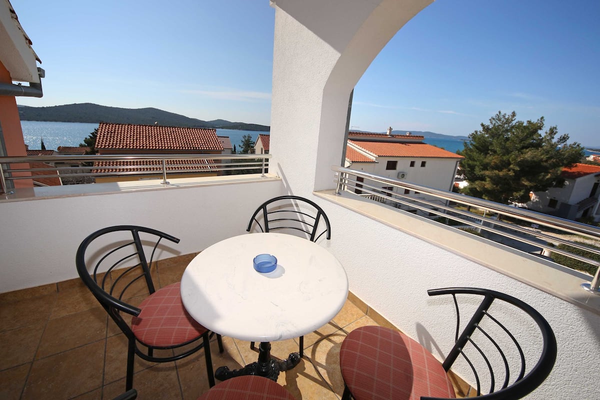 A balcony with a table and chairs, overlooking a body of water and buildings.