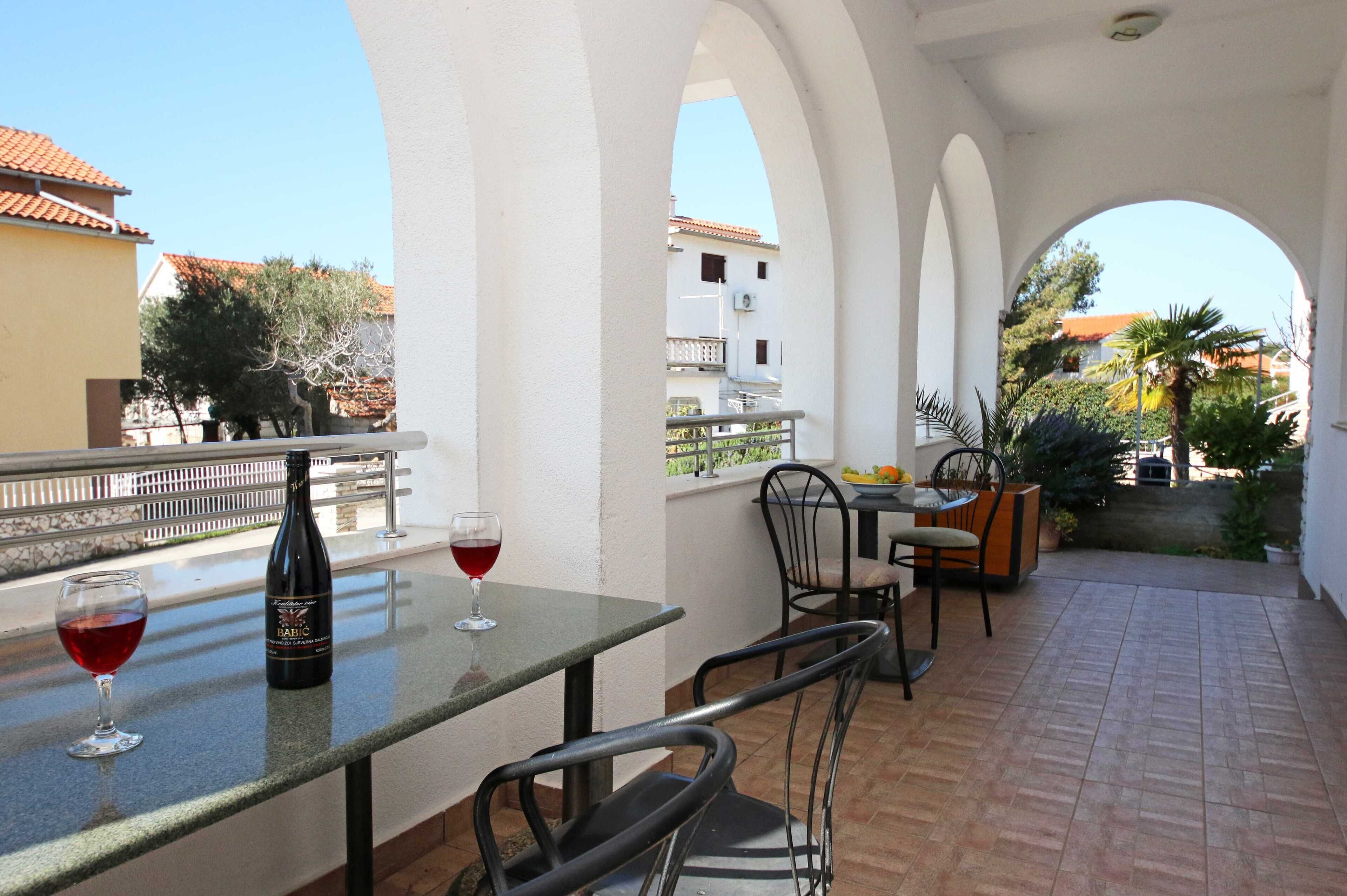 An outdoor patio with a table, chairs, and a bottle of red wine.