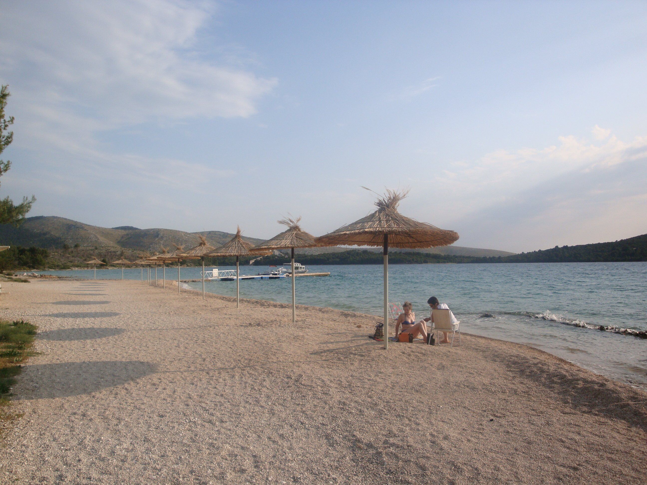 A beach with thatched umbrellas and a boat in the background.
