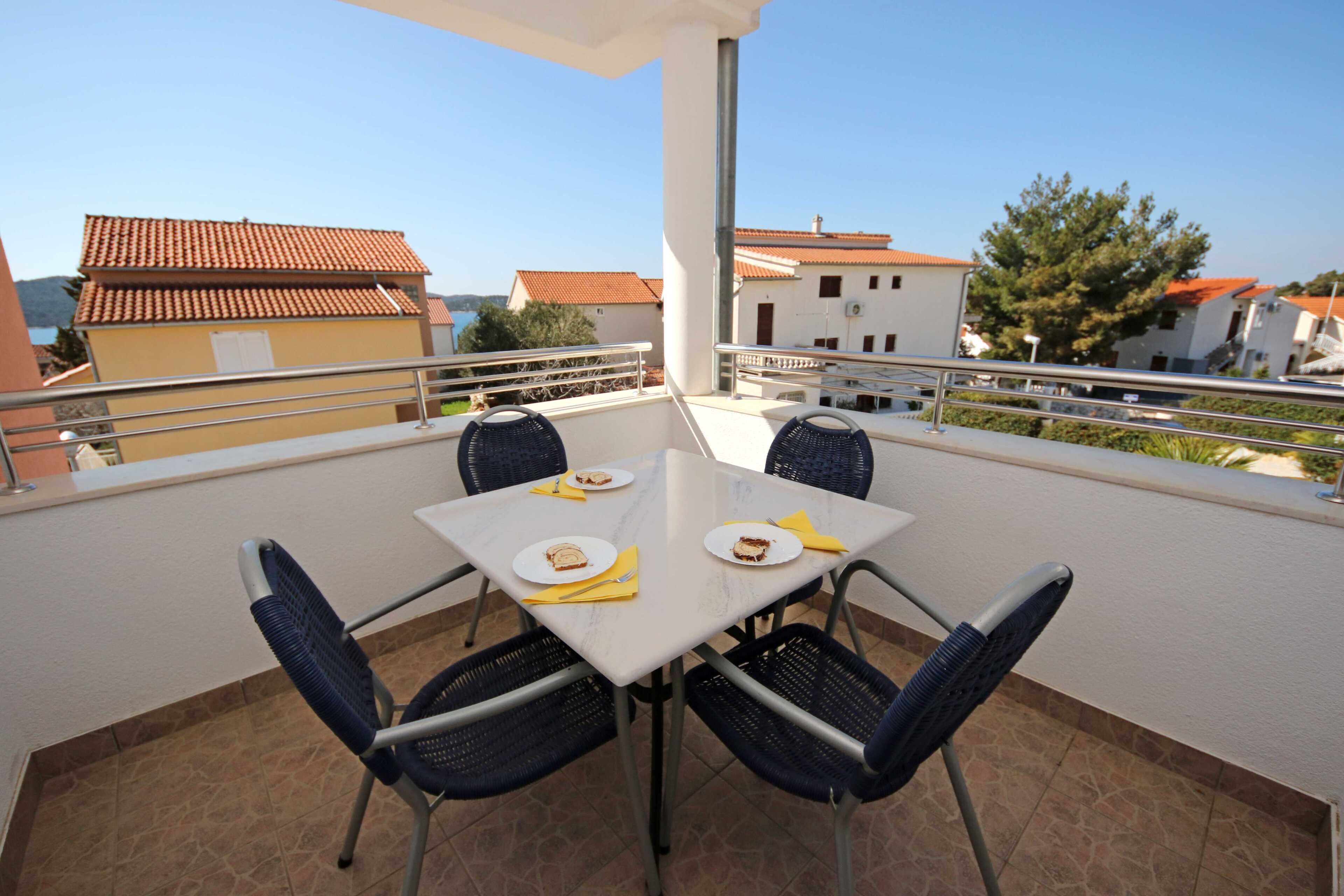 Une terrasse avec une table et des chaises, un sol carrelé et une vue sur les bâtiments et les arbres.