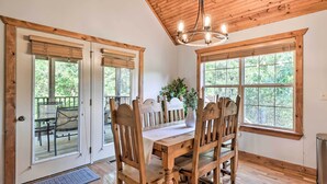 Un comedor con mesa y sillas de madera, ventanas amplias y techo de madera.