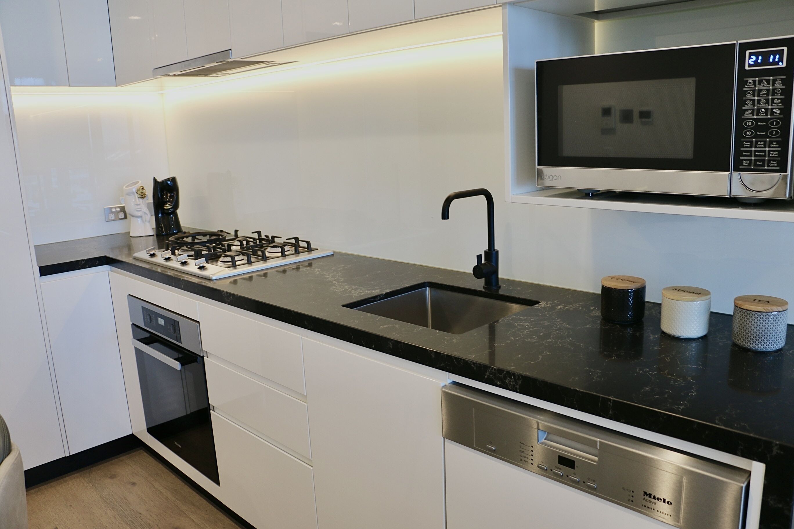 A modern kitchen with white cabinets, a black countertop, a built-in microwave, a gas stove, and a dishwasher.