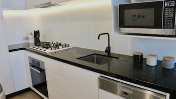 Una cocina moderna con armarios blancos, encimera negra, microondas empotrado, cocina a gas y lavavajillas.