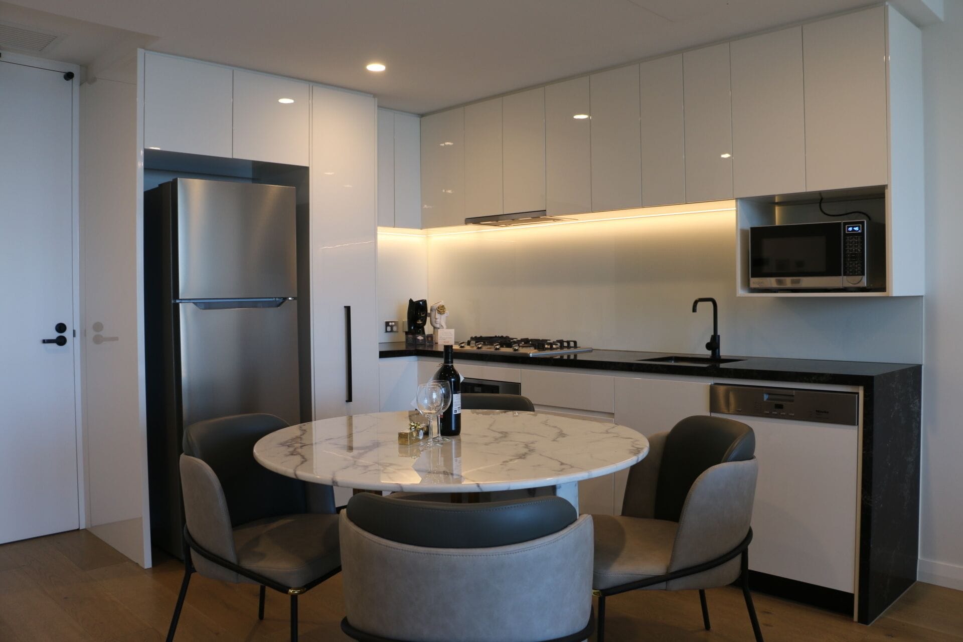 Una cocina moderna con una mesa redonda de mármol, dos sillas, un microondas integrado y un lavavajillas.