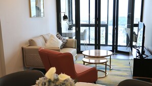 A modern living room with a sofa, armchair, coffee table, and a view of the city through large windows. - Kooii Apartments (Fortitude Valley)