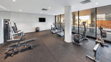 Un gimnasio moderno con varios equipos de ejercicio, un ventanal grande y un televisor de pantalla plana en la pared.