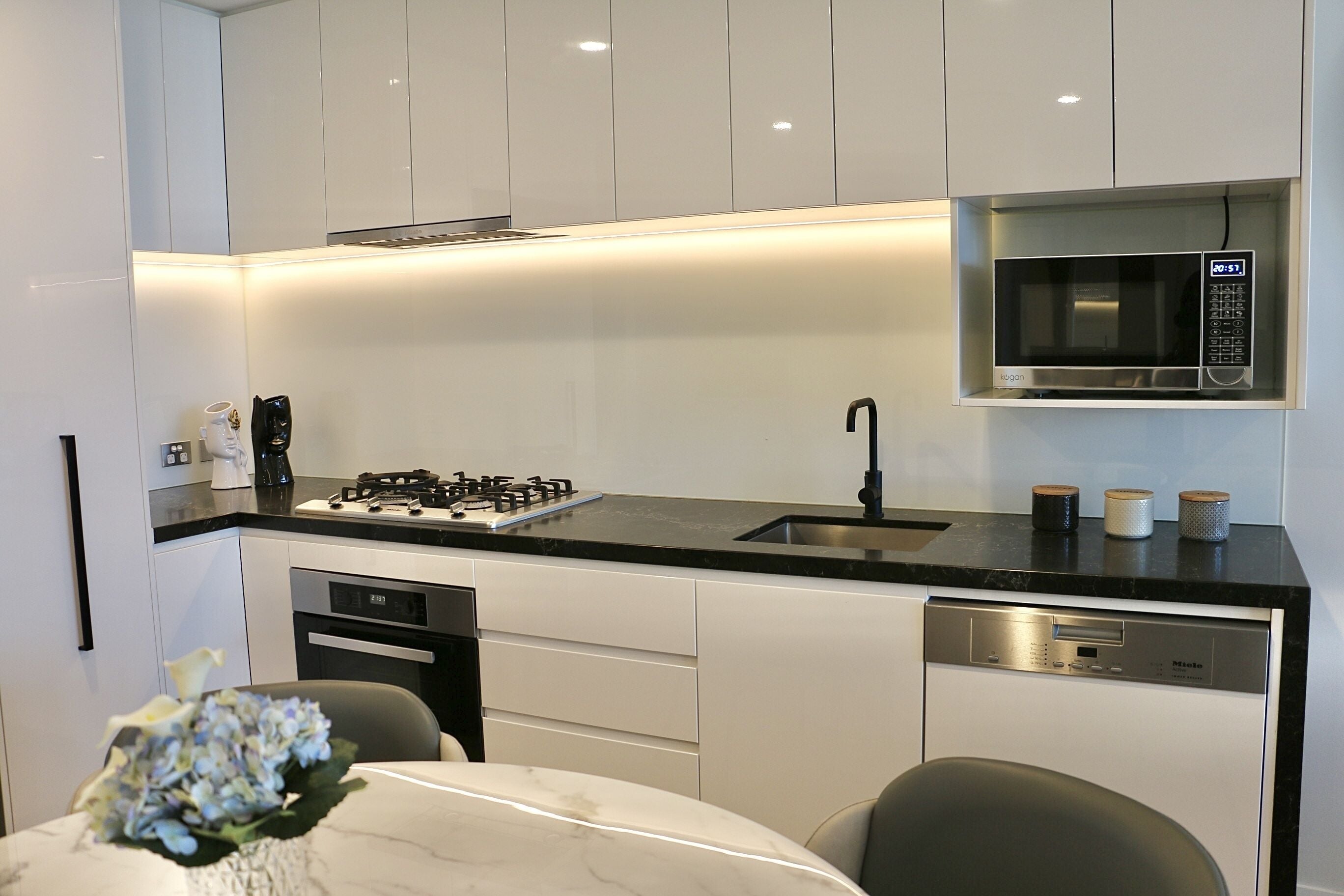 A modern kitchen with white cabinets, a black countertop, a built-in microwave, a dishwasher, and a gas stove.