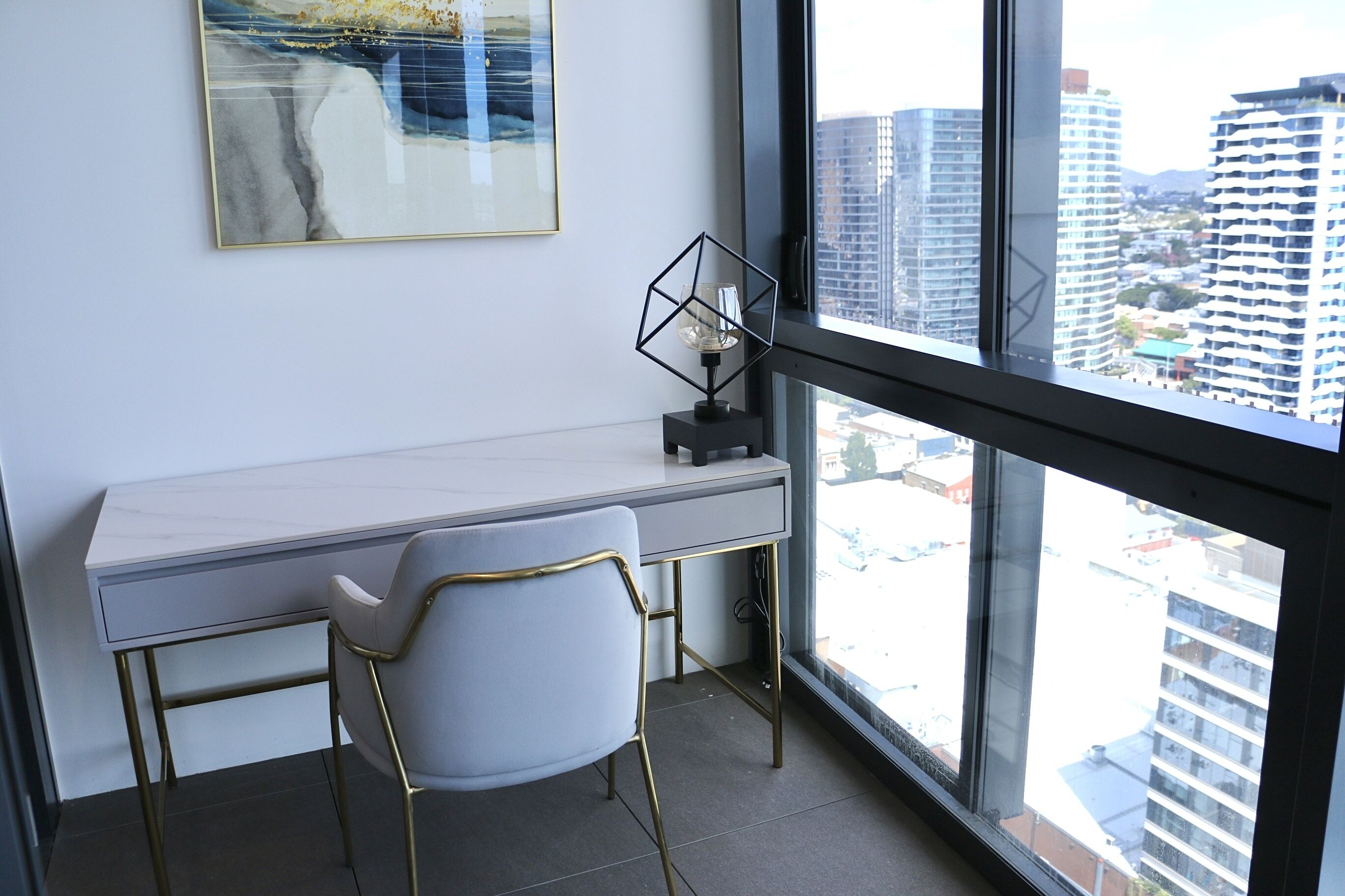 Um espaço de escritório moderno com uma escrivaninha branca, uma cadeira e vista para edifícios altos por uma janela grande.