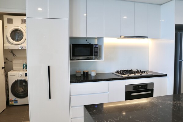 Una cocina moderna con armarios blancos, microondas integrado, cocina a gas y lavadora en la habitación contigua.