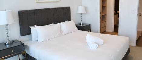A neatly made bed with white linens, a dark headboard, and a bedside table with a lamp.