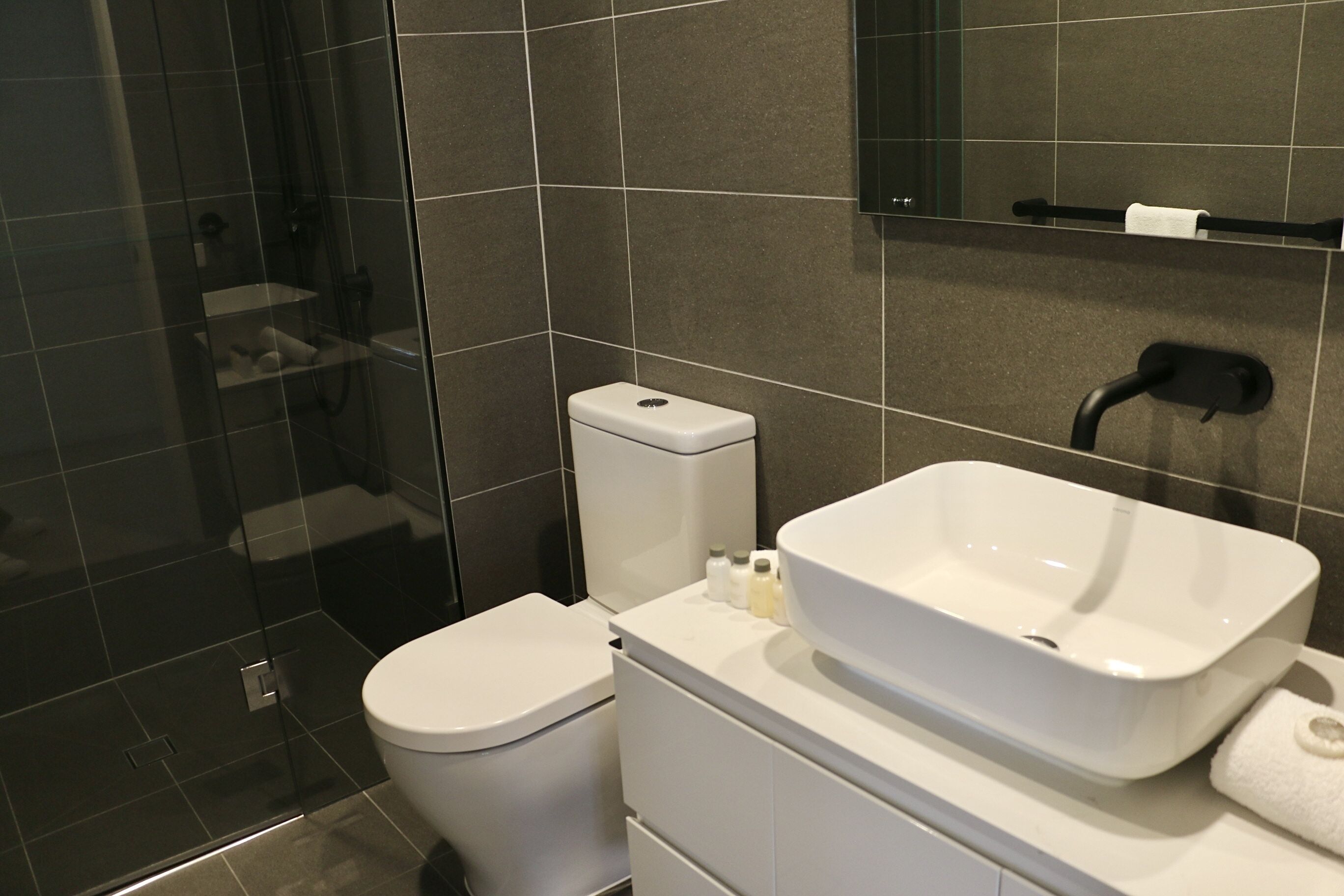 Un baño moderno con cabina de ducha de vidrio, inodoro blanco y un lavamanos grande de color blanco con un espejo encima.