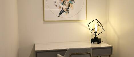 A desk with a lamp, a chair, and a framed artwork on the wall.