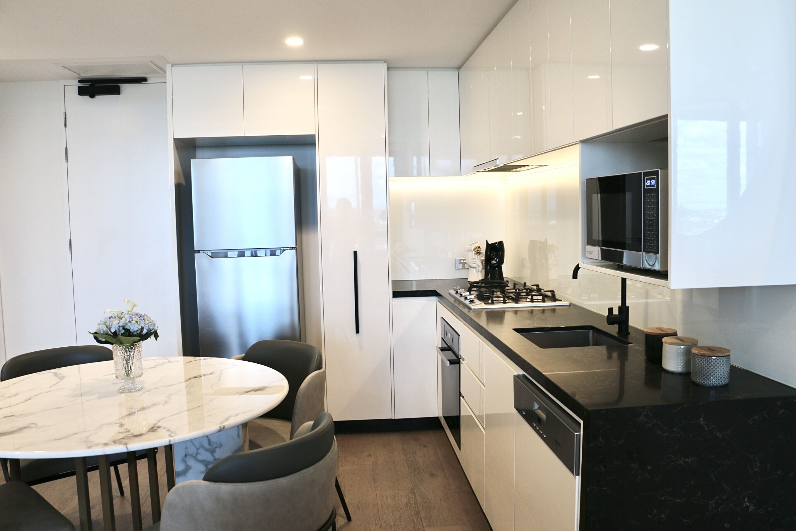 A modern kitchen with white cabinetry, a marble countertop, a built-in microwave, and a gas stove.