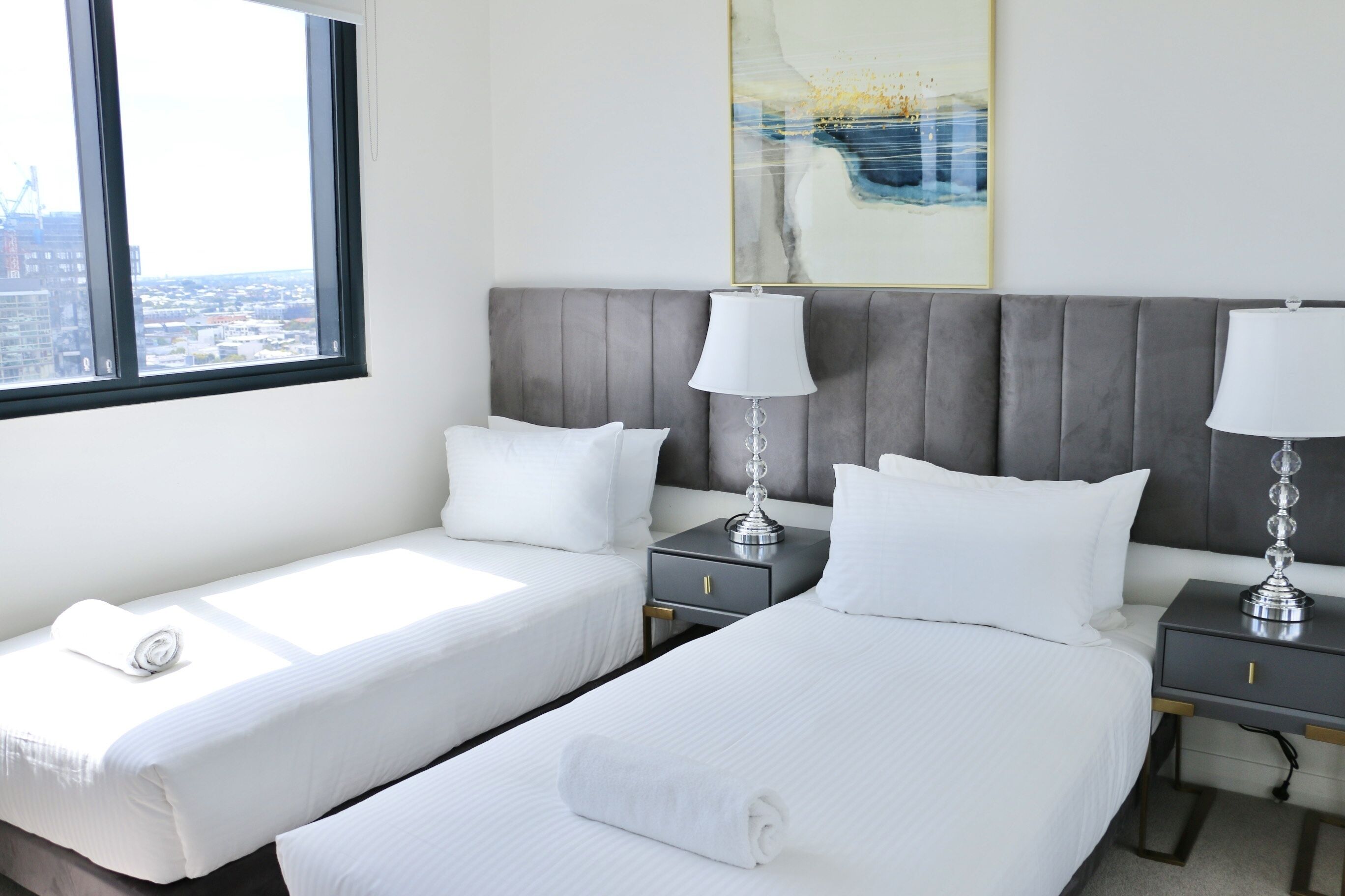 A hotel room with two beds, a large window, and a city view.