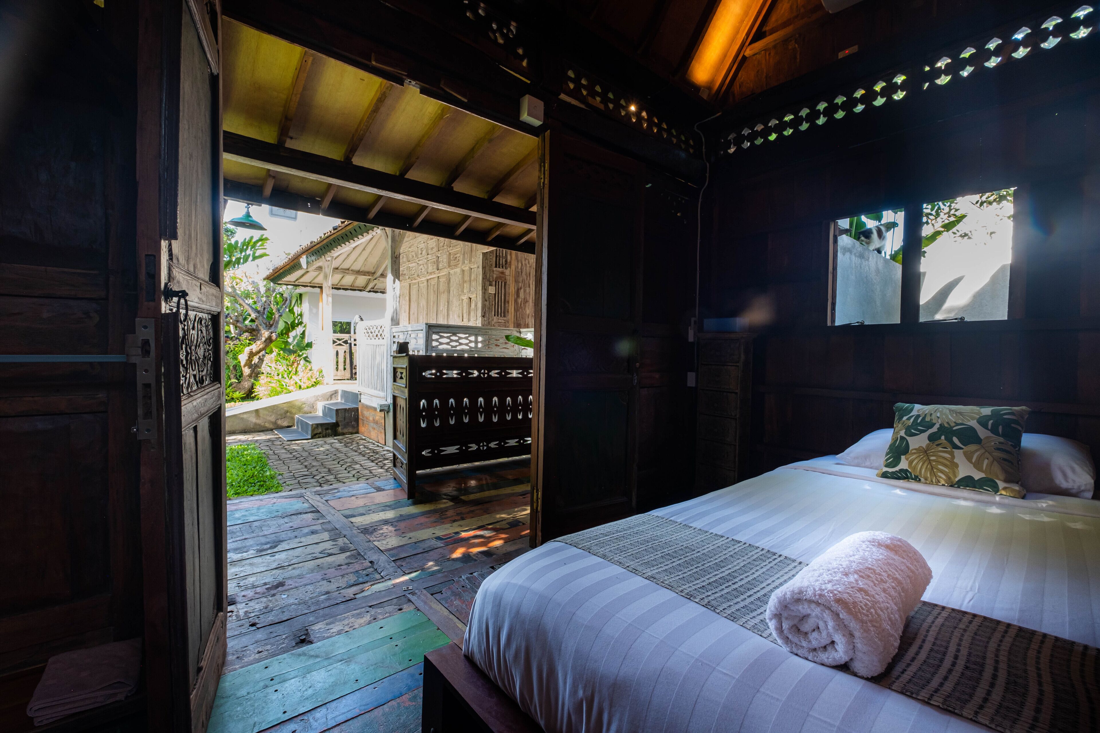 A wooden room with a bed, a window, and a door leading outside.